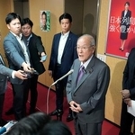 　沖縄県知事選で古謝玄太氏の当選が決まり、記者団の取材に応じる自民党の鈴木幹事長。右端は西村選対委員長＝１３日夜、東京・永田町の党本部