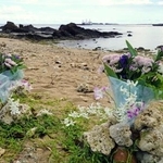　転覆事故の現場海域を臨む浜辺に手向けられた花束＝１６日午後、沖縄県名護市