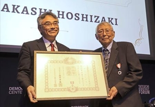 　２３日、室田幸靖駐ロサンゼルス総領事（左）から勲記を手渡されたタカシ・ホシザキさん＝米ロサンゼルス（共同）