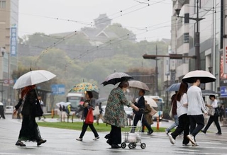　雨が降る中、傘を差して熊本市内を歩く人たち。奥は熊本城＝２６日午前