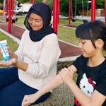 　蚊よけ効果のある「ビオレガード　モスブロックセラム」を使う親子＝マレーシア（提供写真）