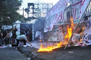　地方議会庁舎の門に竹の棒を投げたり、火を付けたりして抗議する人々＝１日、インドネシア・西ジャワ州（ロイター＝共同）