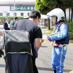 　自転車利用者に注意喚起のチラシを配る警視庁の警察官＝６月、東京都葛飾区