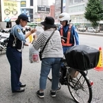 　自転車利用者に啓発用のチラシを配る警察官＝４日午前、東京都新宿区