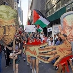 　２６日、米ニューヨークで行われた抗議デモ。トランプ大統領とネタニヤフ首相の似顔絵や、血塗られた手のイラストを持って歩く参加者もいた（共同）