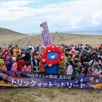 　鳥取砂丘で開かれたハロウィーンパーティーに登場した「ミャクミャク」と記念撮影する参加者＝２６日午後、鳥取市