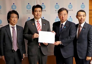 　自民党の「大学病院を支援する議員連盟」の松野博一会長（中央右）から緊急決議を受け取る松本文科相＝１１日午後、文科省