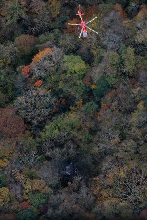 　小型機が墜落したとみられる現場（下）で救助活動を行う消防ヘリ＝１８日午後１時５分、福岡県八女市（共同通信社ヘリから）