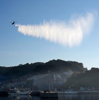 　大分市佐賀関の大規模火災現場付近で上空から放水する自衛隊のヘリコプター＝２０日午前８時４分