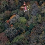 　小型機が墜落したとみられる現場（下）で救助活動を行う消防ヘリ＝１８日午後１時５分、福岡県八女市（共同通信社ヘリから）