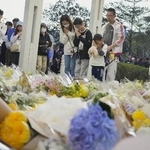 　火災現場の高層住宅群の近くで手を合わせる人たち＝２９日、香港北部・新界地区大埔