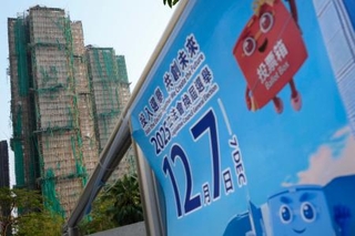 　火災のあった高層住宅群（左奥）の近くに掲示された立法会選挙の投票を呼びかけるポスター＝５日、香港（共同）