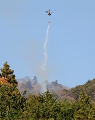 　神奈川県伊勢原市と厚木市にまたがる日向山で散水する消防ヘリコプター＝１０日午前８時１２分