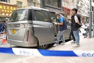 　香港の強盗事件で、近くの路上に残された容疑者が使ったとみられる車を調べる警察官ら＝１８日（共同）