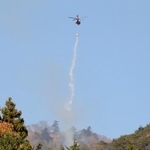 　神奈川県伊勢原市と厚木市にまたがる日向山で散水する消防ヘリコプター＝１０日午前８時１２分