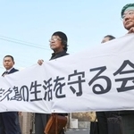 　仮処分の申し立て後、長崎地裁佐世保支部前で横断幕を掲げるＮＰＯ法人「宇久島の生活を守る会」の佐々木浄栄会長（左端）ら＝１９日午後、佐世保市