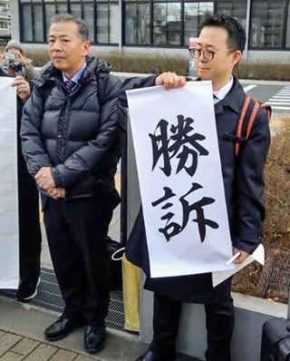 　判決を受け「勝訴」と書かれた垂れ幕の脇に立つ丸尾牧兵庫県議（左）＝２８日午後、兵庫県尼崎市