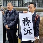 　判決を受け「勝訴」と書かれた垂れ幕の脇に立つ丸尾牧兵庫県議（左）＝２８日午後、兵庫県尼崎市