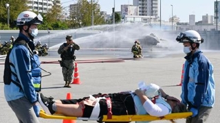 　米軍機墜落事故を想定した訓練で、負傷者を搬送する救急当局者。奥は消火訓練で放水を受ける米軍機＝１９日午前、沖縄県浦添市