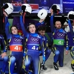 　リュージュのチームリレーで、ゴール後に片膝をついてヘルメットを掲げるウクライナ代表の選手たち＝コルティナダンペッツォ（ロイター＝共同）