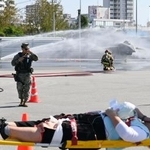 　米軍機墜落事故を想定した訓練で、負傷者を搬送する救急当局者。奥は消火訓練で放水を受ける米軍機＝１９日午前、沖縄県浦添市