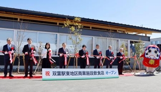 　ＪＲ双葉駅前に完成した商業施設のオープニングセレモニーで、テープカットする伊沢史朗町長（左から４人目）ら＝１４日午前、福島県双葉町
