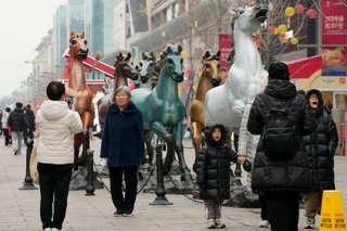 　北京市内の繁華街に置かれた馬の模型の前で写真を撮る人たち＝２月（共同）