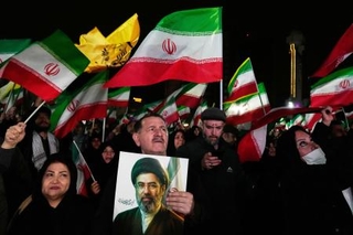　イラン新最高指導者モジタバ・ハメネイ師の写真を持つ支持者ら＝２５日、テヘラン（ＡＰ＝共同）
