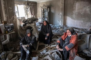 　イランの首都テヘランで、攻撃で壊れた住宅のがれきの上に座り込む住民たち＝３０日（ゲッティ＝共同）