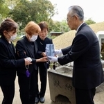 　１３歳で被爆して亡くなった梶山初枝さんの遺骨を受け取る妹の美智子さん（左から２人目）。右奥は原爆供養塔＝２２日午前、広島市の平和記念公園