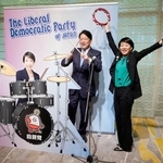 　自民党大会の会場に設置された高市首相のフォトパネルの横でポーズをとる小野寺五典税調会長（左）と鈴木貴子広報本部長＝１２日午前、東京都内