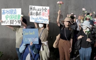 　米軍嘉手納基地のゲート前で、花を手に性暴力の撲滅を訴える「フラワーデモ」の参加者＝６月