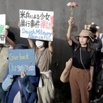 　米軍嘉手納基地のゲート前で、花を手に性暴力の撲滅を訴える「フラワーデモ」の参加者＝６月