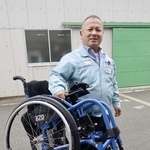 軽量車いすを片手で持ち上げる橋本エンジニアリングの橋本裕司社長＝浜松市