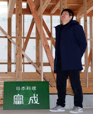 　骨組みのまま工事がストップしている日本料理店「富成」の新店舗建設地に立つ冨成寿明さん＝２０２５年２月、石川県輪島市町野町