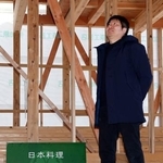 　骨組みのまま工事がストップしている日本料理店「富成」の新店舗建設地に立つ冨成寿明さん＝２０２５年２月、石川県輪島市町野町
