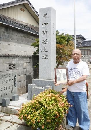 　「模擬原爆」の犠牲者を追悼する慰霊碑の前で、父善蔵さんの写真を持つ鈴木善作さん＝７月１８日、富山市