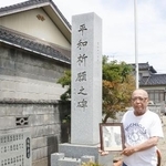 　「模擬原爆」の犠牲者を追悼する慰霊碑の前で、父善蔵さんの写真を持つ鈴木善作さん＝７月１８日、富山市
