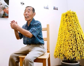 　展覧会の会場で自身の作品と写真に納まる北三郎さん（仮名）＝３日、東京都内