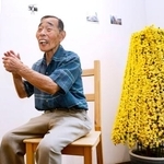 　展覧会の会場で自身の作品と写真に納まる北三郎さん（仮名）＝３日、東京都内