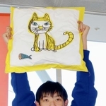 　自身が描いたネコがプリントされたクッションを掲げるぽんちゃん＝２０２５年１１月、前橋市