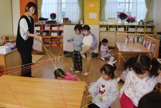 　芸術士の長野由美さん（左端）と蓄光のゴムひもを結び付ける園児たち＝２０２５年１２月１６日、高松市のカナン十河こども園