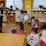 　芸術士の長野由美さん（左端）と蓄光のゴムひもを結び付ける園児たち＝２０２５年１２月１６日、高松市のカナン十河こども園