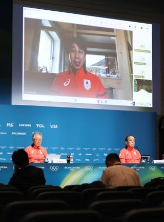 　記者会見する日本選手団の伊東秀仁団長（左）ら。大型モニターはオンラインで出席した原田雅彦副団長＝１３日、イタリア・ミラノ（共同）