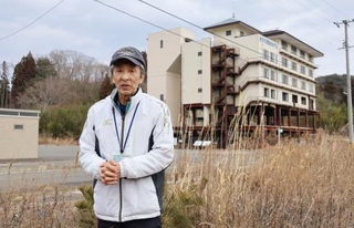 　「たろう観光ホテル」（奥）近くの自宅跡地に立つ小幡実さん＝５日、岩手県宮古市