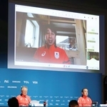 　記者会見する日本選手団の伊東秀仁団長（左）ら。大型モニターはオンラインで出席した原田雅彦副団長＝１３日、イタリア・ミラノ（共同）