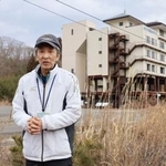 　「たろう観光ホテル」（奥）近くの自宅跡地に立つ小幡実さん＝５日、岩手県宮古市