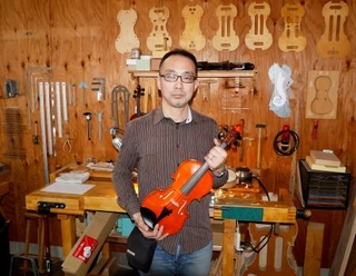 　工房でバイオリンを持つ池尻雅博さん＝２０２６年２月、愛知県一宮市