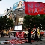 ＪＲ新宿駅東南口で「ＮＯ　ＨＡＴＥ」と書かれた旗を振る鍋倉雅之さん＝５月
