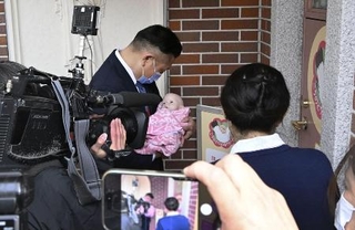 熊本市の慈恵病院を視察し、赤ちゃんポスト前で赤ちゃんの人形を抱く大阪府泉佐野市の千代松大耕市長（奥）＝２月